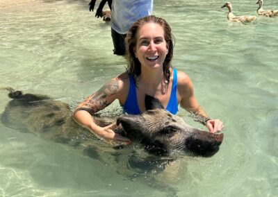 An image of a woman in the water with a pig in the waters of the Bahamas.